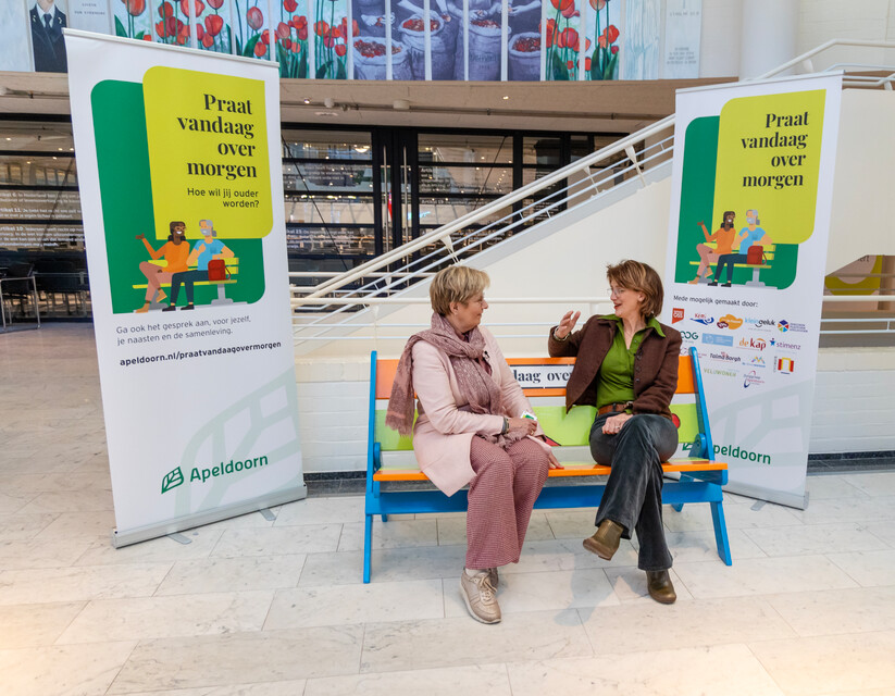 Wethouder Anja Prins en Lineke zitten op een bankje en praten met elkaar.